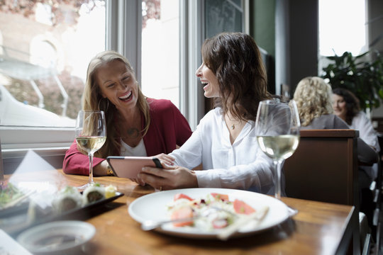 Women friends with smart phone drinking wine and eating sushi, dining at restaurant