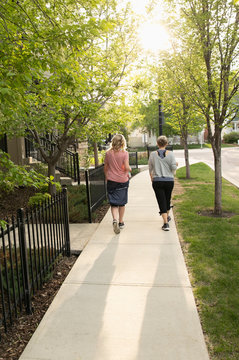 Senior female friends walking, exercising on neighborhood sidewalk