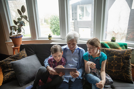 Grandmother and granddaughters using digital tablet on sofa
