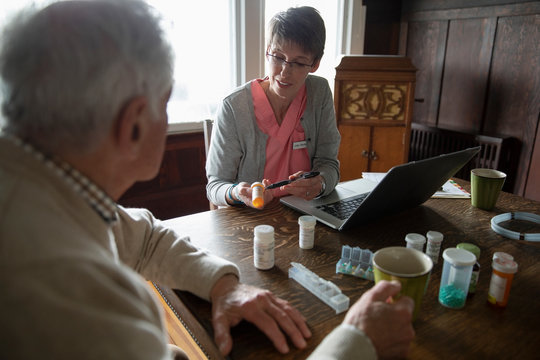 Home caregiver explaining prescription medication to senior man at dining table