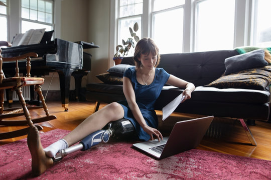 Young woman amputee using laptop on living room floor