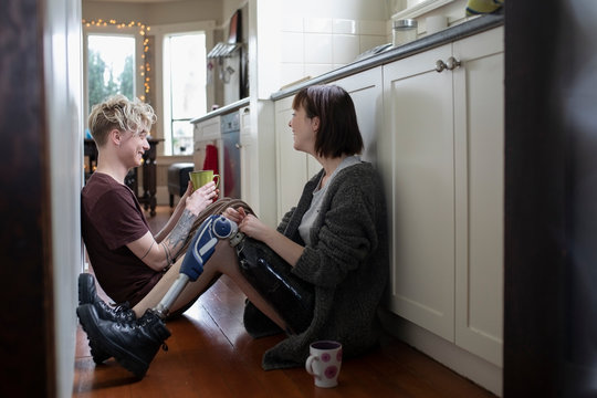 Young woman amputee drinking coffee, talking with boyfriend on kitchen floor