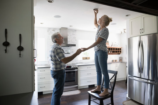 Senior Father Helping Daughter Changing Light Bulb In Kitchen