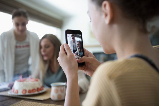 Teenage girl with camera phone photographing mother and sister with birthday cake