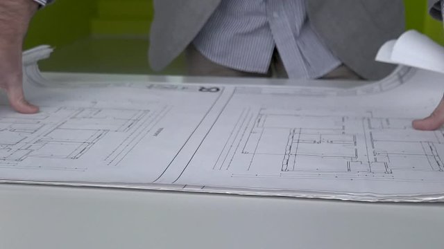 Hombre arquitecto abre planos de construcción sobre mesa HD