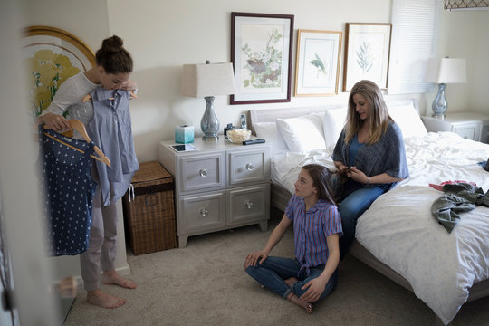 Mother helping teenage daughters with hair and clothing in bedroom