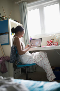 Teenage girl texting with smart phone at desk in bedroom
