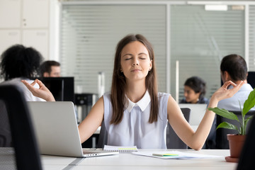 Young female employee meditate managing stress at workplace