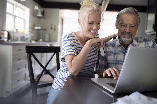 Smiling, affectionate daughter helping senior father using laptop