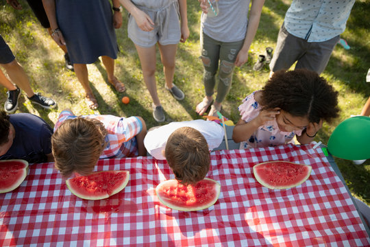 Kids Enjoying Watermelon Eating Contest At Summer Neighborhood Block Party In Park