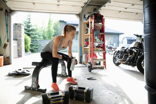 Young woman weightlifting, resting in garage