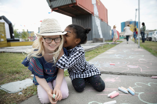 Girls whispering secret, coloring with sidewalk chalk