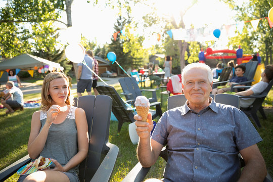 Portrait carefree senior man eating ice cream cone with daughter at summer neighborhood block party in park