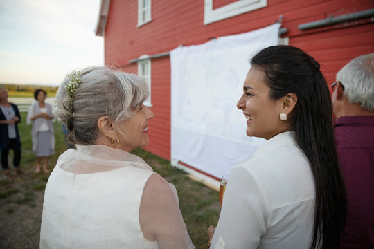 Senior Bride And Friend Enjoying Slideshow Presentation On Barn Wall