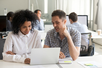 Multiracial colleagues busy working on laptop in office together