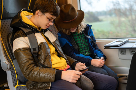 Teenager two boy in a yellow jacket with phones in hand sitting in a suburban train watching a video on a mobile phone. Gadget addiction. Family vacation with young generation 