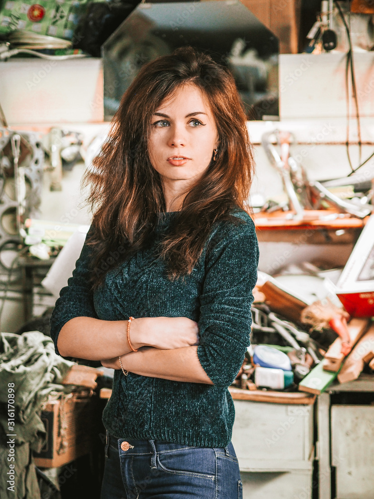 Wall mural A brunette girl with long hair in a green jacket stands in the workshop against the background of tools