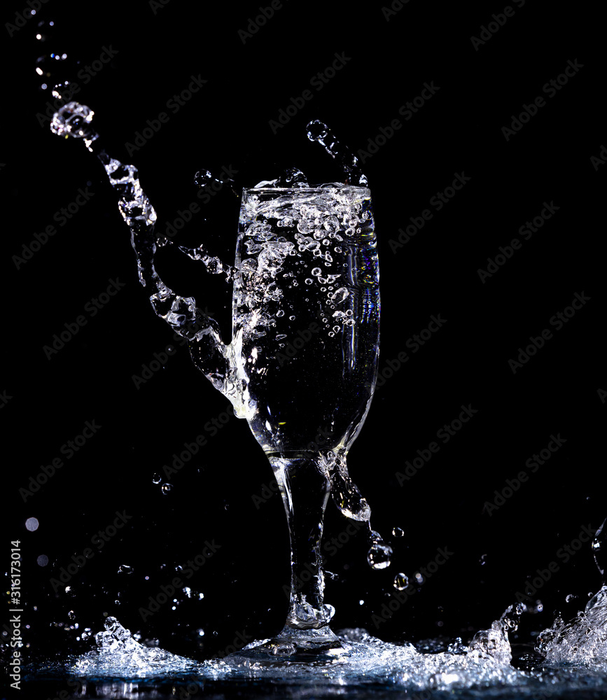 Wall mural Water with splashes in a glass on a black background