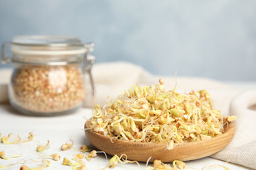 Plate of sprouted green buckwheat on white wooden table, closeup