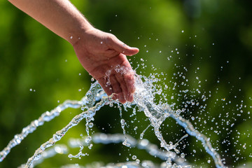 Hand of a man in the spray of water of the fountain