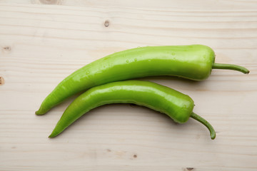 Two green peppers on a wooden background.