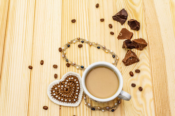 Valentine's Day concept. Cup of coffee, chocolate, knitted heart, string of pearl beads. Romantic breakfast and gift on wooden boards background, copy space