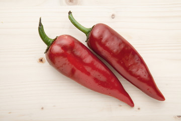 Two red peppers on a wooden background.
