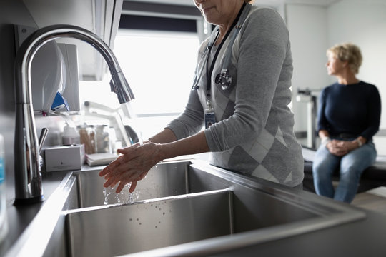 Female doctor washing hands at sink in clinic examination room