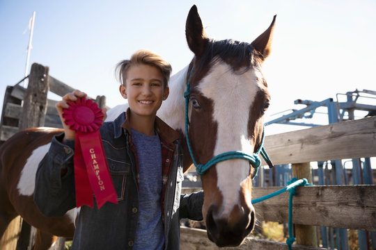 Portrait confident boy with horse holding red champion ribbon