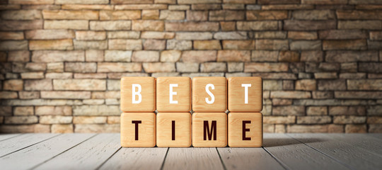 cubes with the words BEST TIME in front of a brick wall on wooden surface