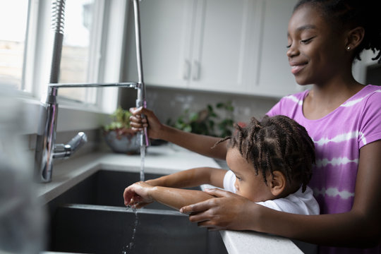 Sister helping her brother to wash hands in kitchen sink