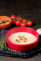 Bowl of mushroom cream soup with fried champignon mushrooms and vegetables on black stone background. Rustic style. Close up.