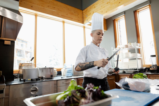 Female chef with tattoos sharpening knife in restaurant kitchen