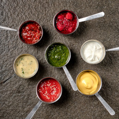 Set of different sauces - ketchup, mayonnaise, barbecue, berry jam, sour cream, pesto, chili, tomato, adzhika, tkemali sauce on black stone background. Top view copy space