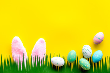 Easter concept. Eggs, Bunny's ears and grass on yellow background top-down copy space