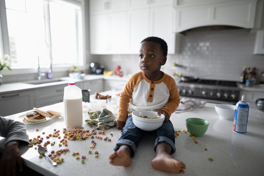 Cute, Messy Toddler Boy Eating Cereal On Kitchen Island