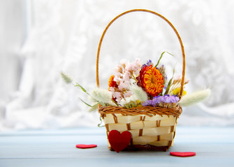 Fototapeta na wymiar A basket of dried flowers and red hearts on a blue tabletop