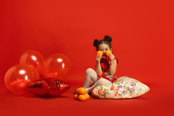 Obraz na płótnie Canvas Balloons and mandarines for mood. Posing cute. Happy Chinese New Year 2020. Asian cute little girl isolated on red background in traditional clothing. Celebration, human emotions, holidays. Copyspace.