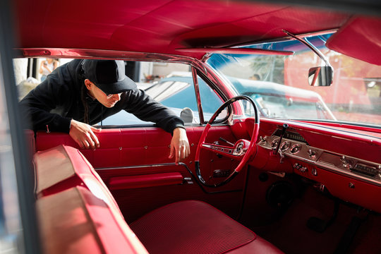 Latinx young man checking out red leather interior of vintage car