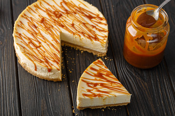 caramel cheesecake, jar and spoon with caramel on a dark wooden background