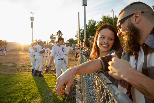 Father And Daughter Talking, Watching Baseball Game At Fence