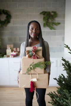 Portrait smiling young woman carrying stack of Christmas gifts