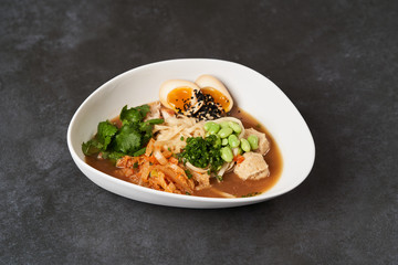 Ramen noodle soup with chicken, shiitake mushroms and egg in a white bowl, top view