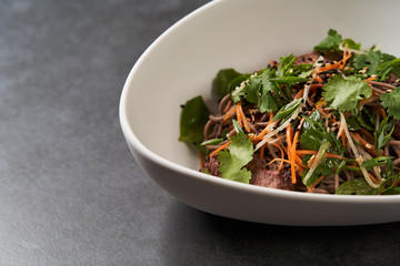 Thai style warm soba salad in white bowl on gray table background