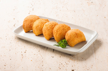 Five rissoles, a small patty enclosed in pastry, or rolled in breadcrumbs, usually baked or deep fried, filled with savory ingredients. On a white plate.