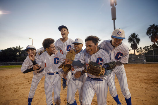 Excited baseball team celebrating win on field at night