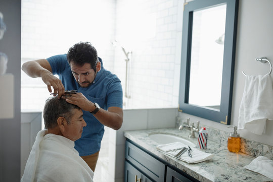 Latinx Son Cutting Senior Father Hair In Bathroom