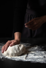 Female hands kneading fresh dough on a black table. Heart drawn on flour. Preparing homemade dough. Cooking with love concept. Low key, dark background, copy space