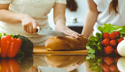 Closeup of human hands cooking in kitchen. Mother and daughter or two female friends cutting bread for dinner. Friendship, family and lifestyle concepts