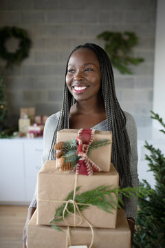 Happy young African American woman holding stack of Christmas gifts